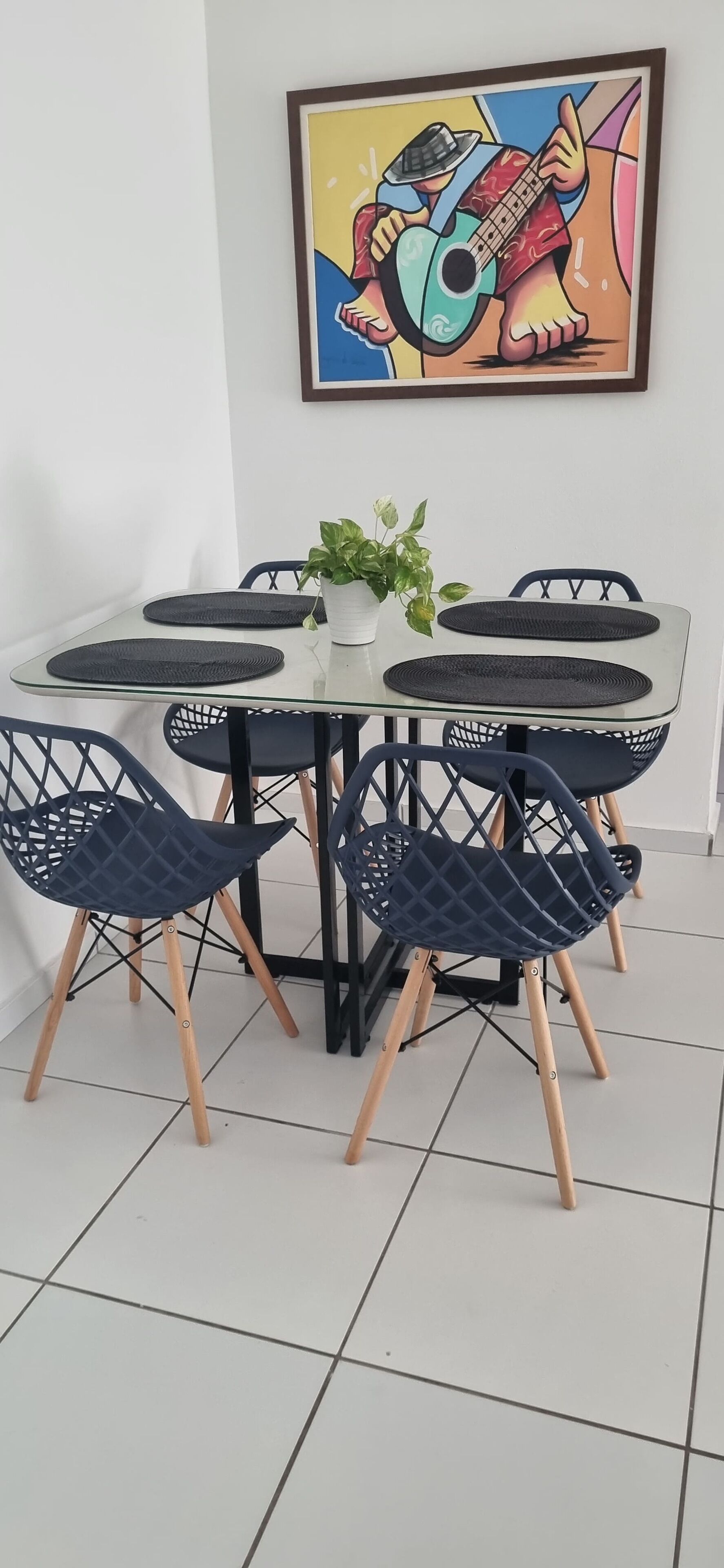 Ein Essbereich mit einem Glastisch, schwarzen gewebten Platzsets und blauen Stühlen mit Holzböcken.