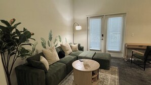 Un salon avec un canapé vert, une table basse ronde et une grande plante.