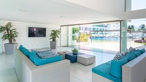 Eine moderne Hotellobby mit großem Fernseher, bequemen Sitzgelegenheiten und Blick auf Pool und Gebäude.