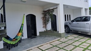 Un bâtiment blanc doté d’une terrasse carrelée, d’un hamac et d’un véhicule garé.