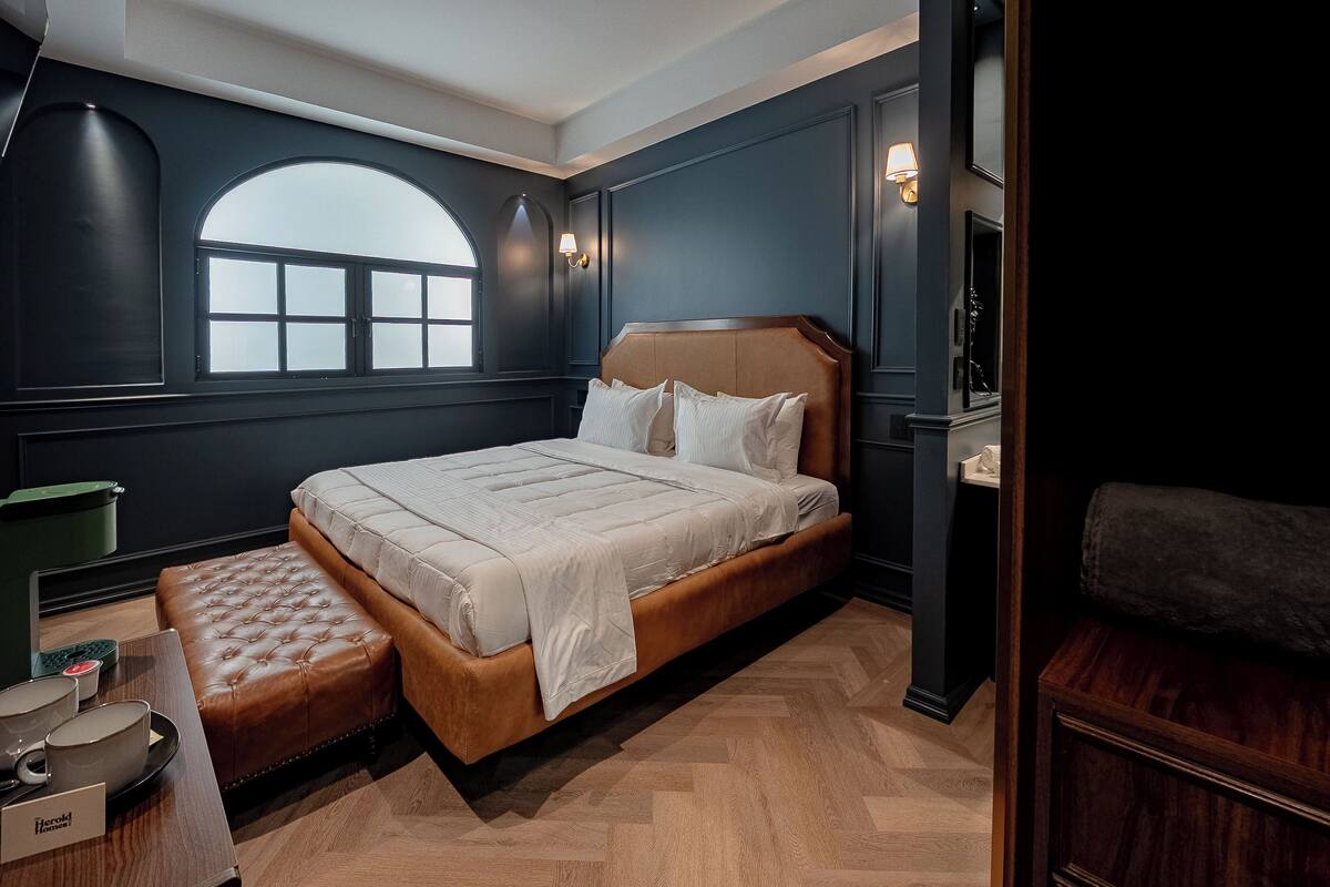A bedroom with a large bed, a bench, a window, and a nightstand.