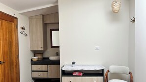 A bedroom with a wooden door, a bed, a dresser, a chair, a hanging light fixture, and a small table with a basket and a pink item. - Casa Corrales by Wynwood House (Andahuaylillas)