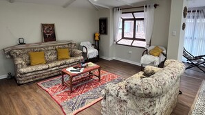 A living room with a sofa, armchair, and a coffee table. There is a window with curtains, a painting on the wall, and a patterned rug on the floor. - Casa Corrales by Wynwood House (Andahuaylillas)