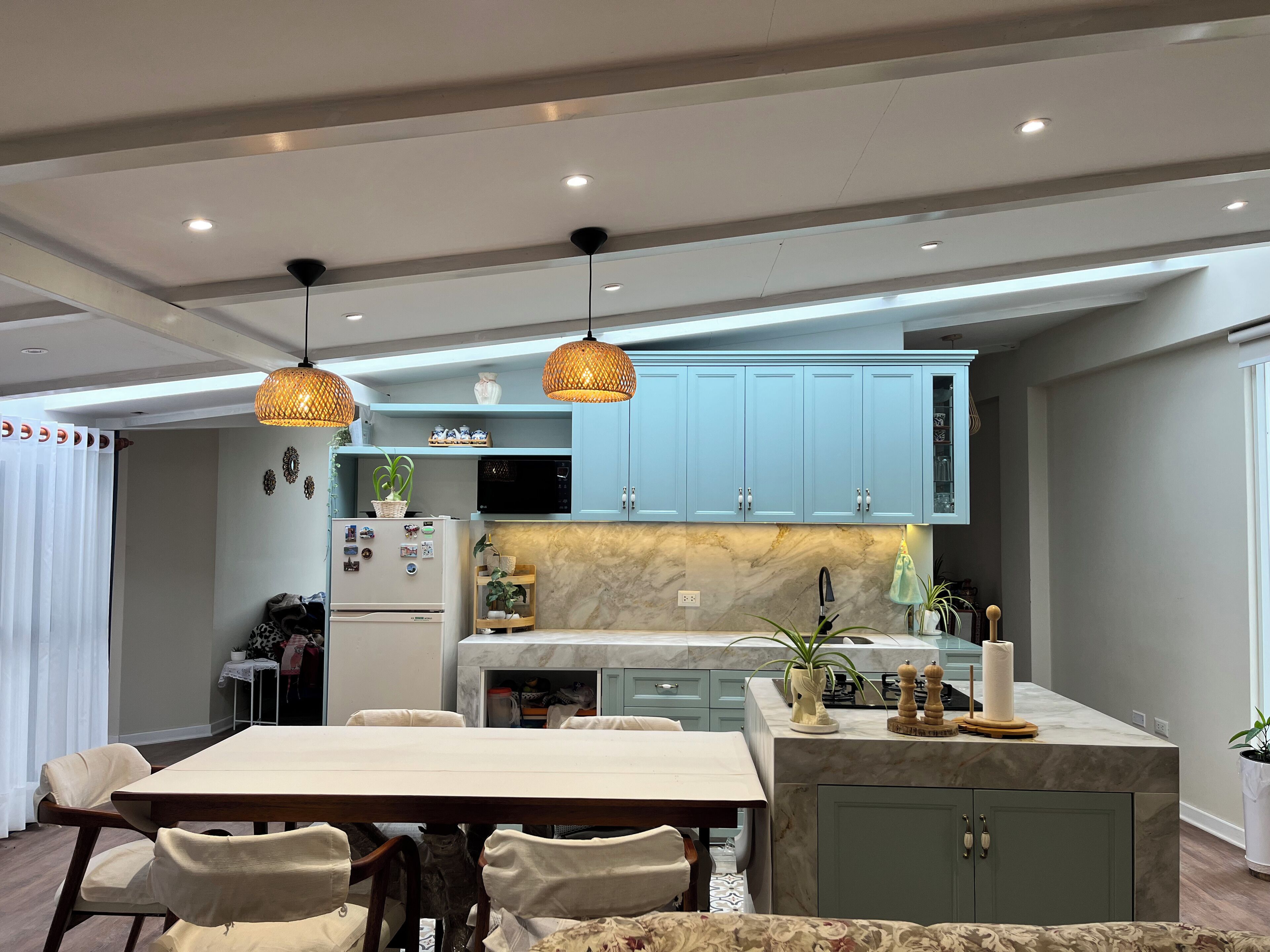 A modern kitchen with light blue cabinets, a marble countertop, and pendant lighting.