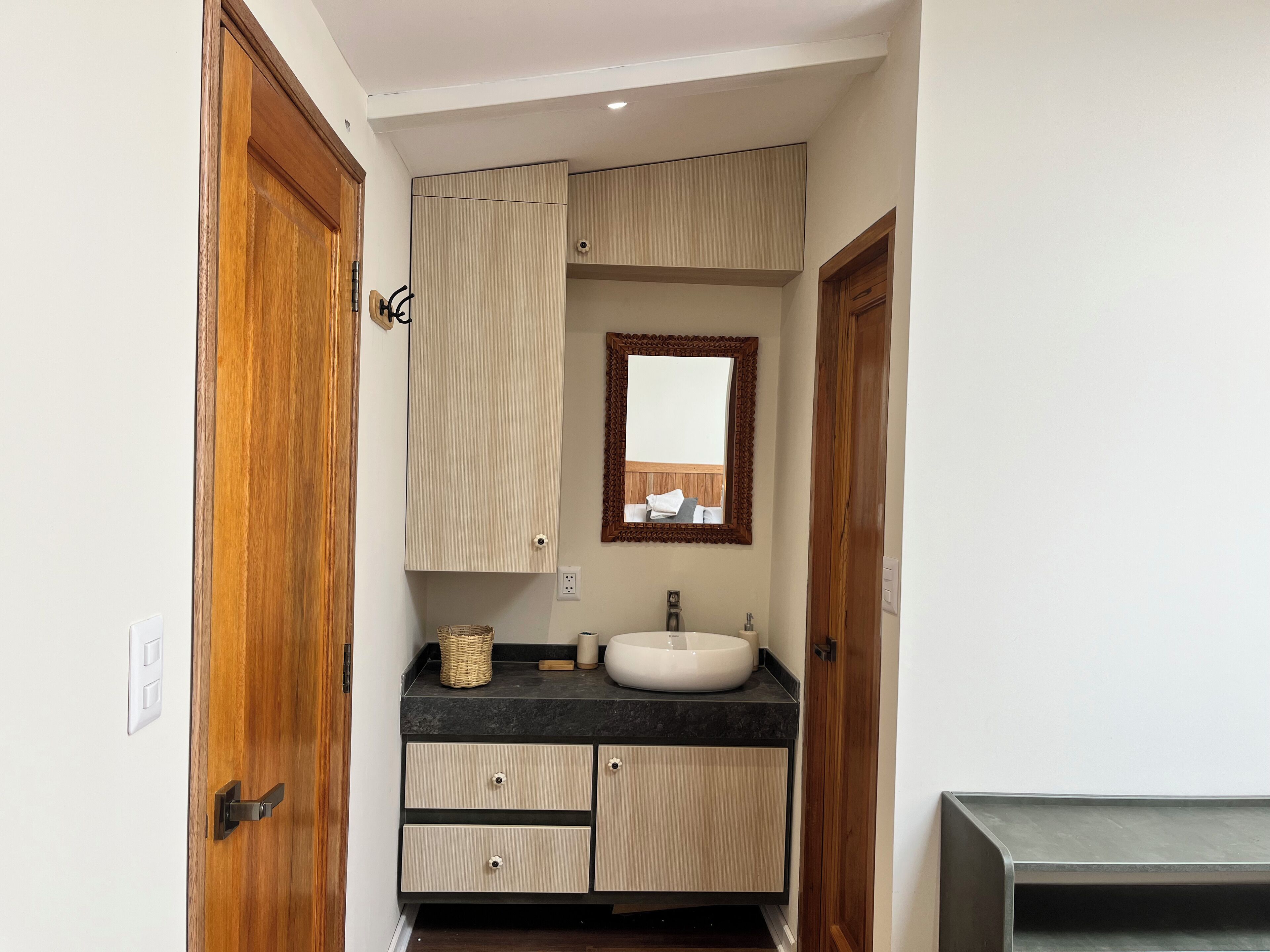 A compact bathroom with a wooden vanity, a round sink, and a mirror with a decorative frame.