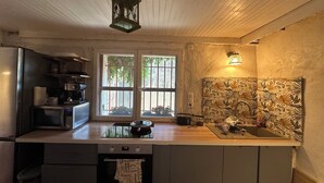Uma cozinha com teto de madeira, janela com vista para o verde, micro-ondas, chaleira e pia com painel decorativo.