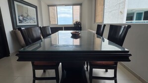 Een eethoek met een glazen tafel, zwarte stoelen, een plafondventilator en een groot raam met uitzicht.
