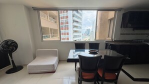 Een compacte woonruimte met een eethoek, kitchenette en een groot raam met uitzicht over de stad.