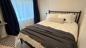 Un dormitorio con cama, puerta, ventana con cortinas y una alfombra.