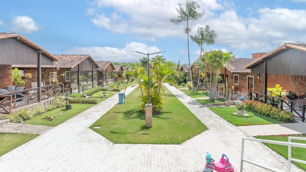 Une rangée de logements de style bungalow, disposés de part et d’autre d’un chemin central, et entourés de jardins bien entretenus et de palmiers.