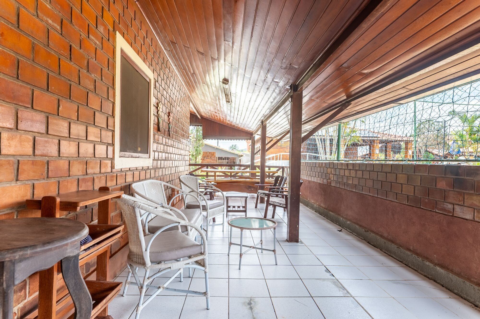 A covered patio area with brick walls, white wicker furniture, and a tiled floor.