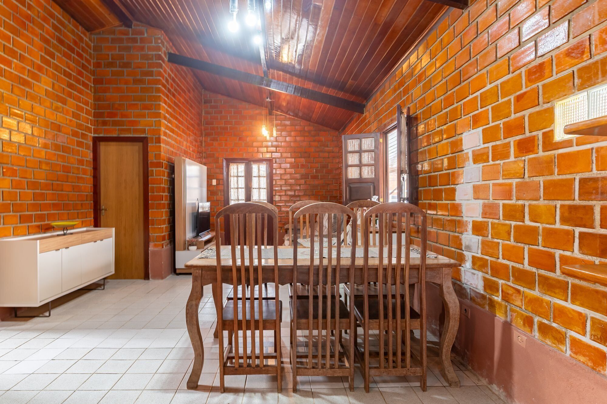 Uma área de refeições com parede de tijolos, teto de madeira e uma mesa com cadeiras.