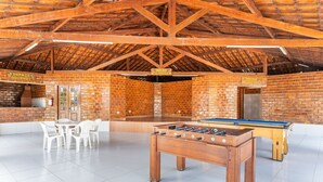 Un espace de loisirs intérieur comprenant une table de baby-foot, un mur en briques et un panneau indiquant « ESPAÇO GOURMET ».
