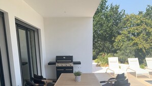 Eine Terrasse im Freien mit einem Holztisch und -stühlen, einem Grill und Blick auf Bäume.