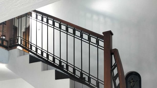 Una escalera con barandilla de madera y balaustres de metal negro, que conduce a un rellano con dos puertas de madera y piso de cuadros.
