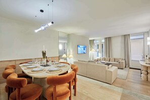 Ein modernes Hotelzimmer mit Essbereich, der einen runden Tisch, bequeme orangefarbene Stühle und einen großen Spiegel beinhaltet.
