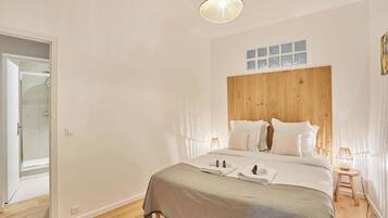 A bedroom with a wooden headboard, a bed with white linens, a bedside table with a lamp, and a door leading to a bathroom.