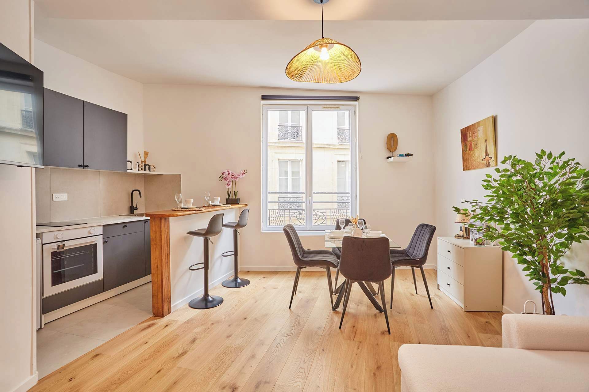 A compact kitchen with a dining area, a large window, and a hanging light fixture.
