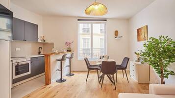 A compact kitchen with a dining area, a large window, and a hanging light fixture.