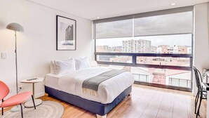 Une chambre moderne avec une grande fenêtre, un lit, une petite table, une chaise et une lampe sur pied.