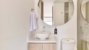 Une salle de bain moderne avec un miroir rond, un lavabo blanc et des toilettes.