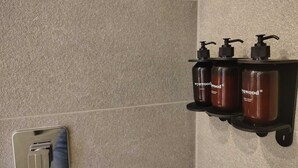 Un baño con repisa empotrada que sostiene tres botellas de productos Wynwood, un secador de manos y un perchero.