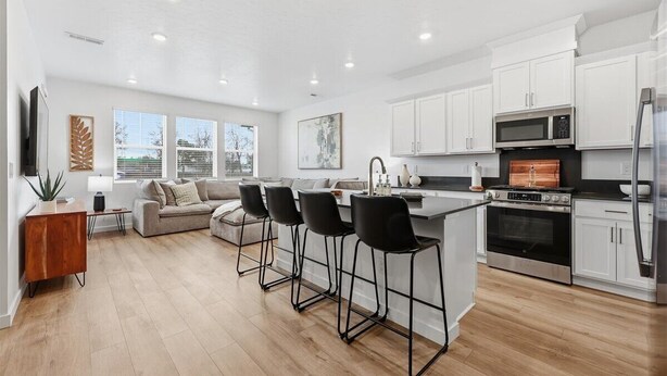 A modern kitchen with white cabinets, a stainless steel oven, and a black countertop. There are four black bar stools and a grey sofa in the living area. - Near Eagle Island | Pool | 2 King Beds | Parking | Smart TV (Eagle)