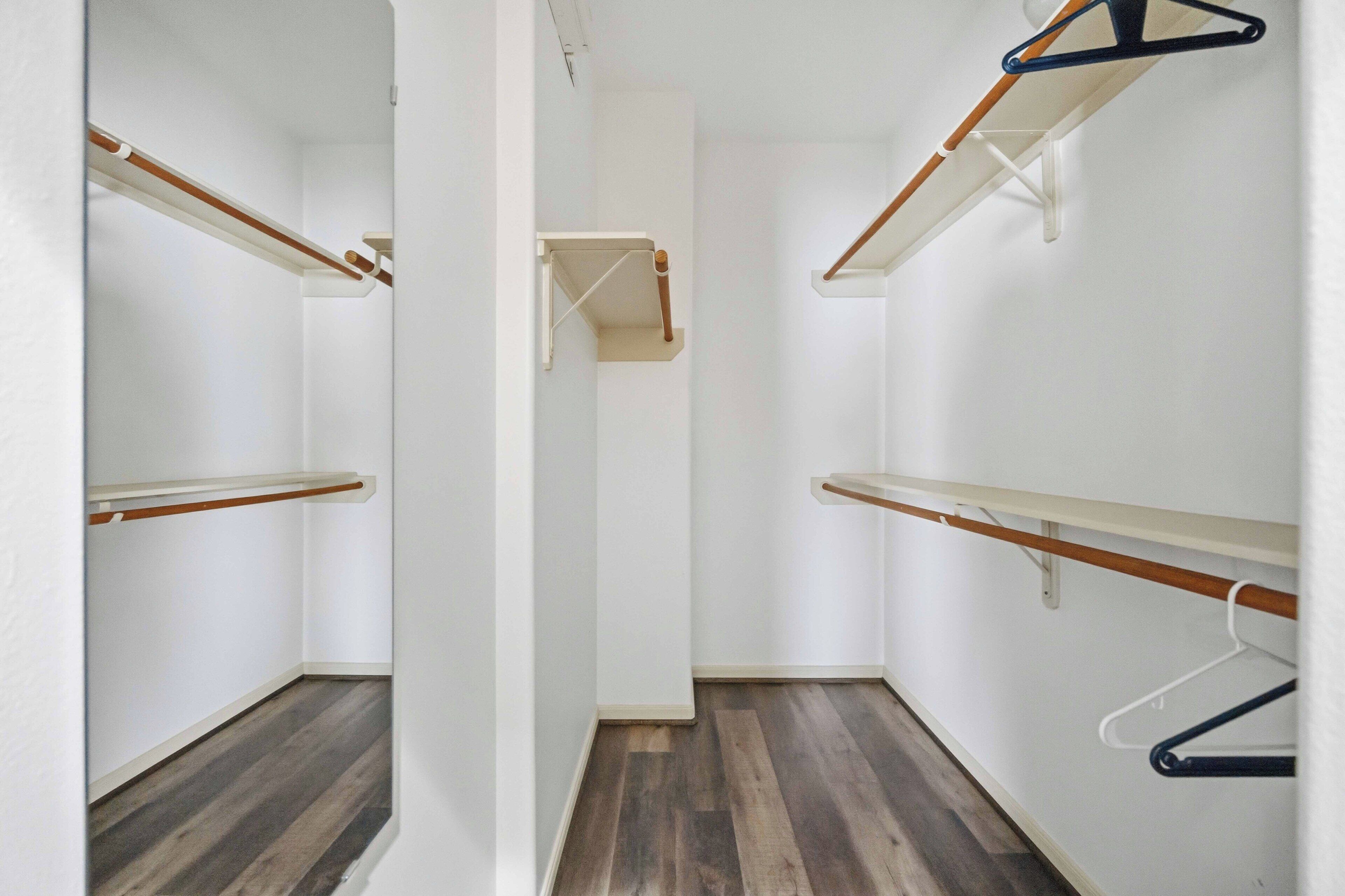 Un pasillo estrecho con suelo de madera y paredes blancas, con un armario de madera con perchas y una pequeña repisa.