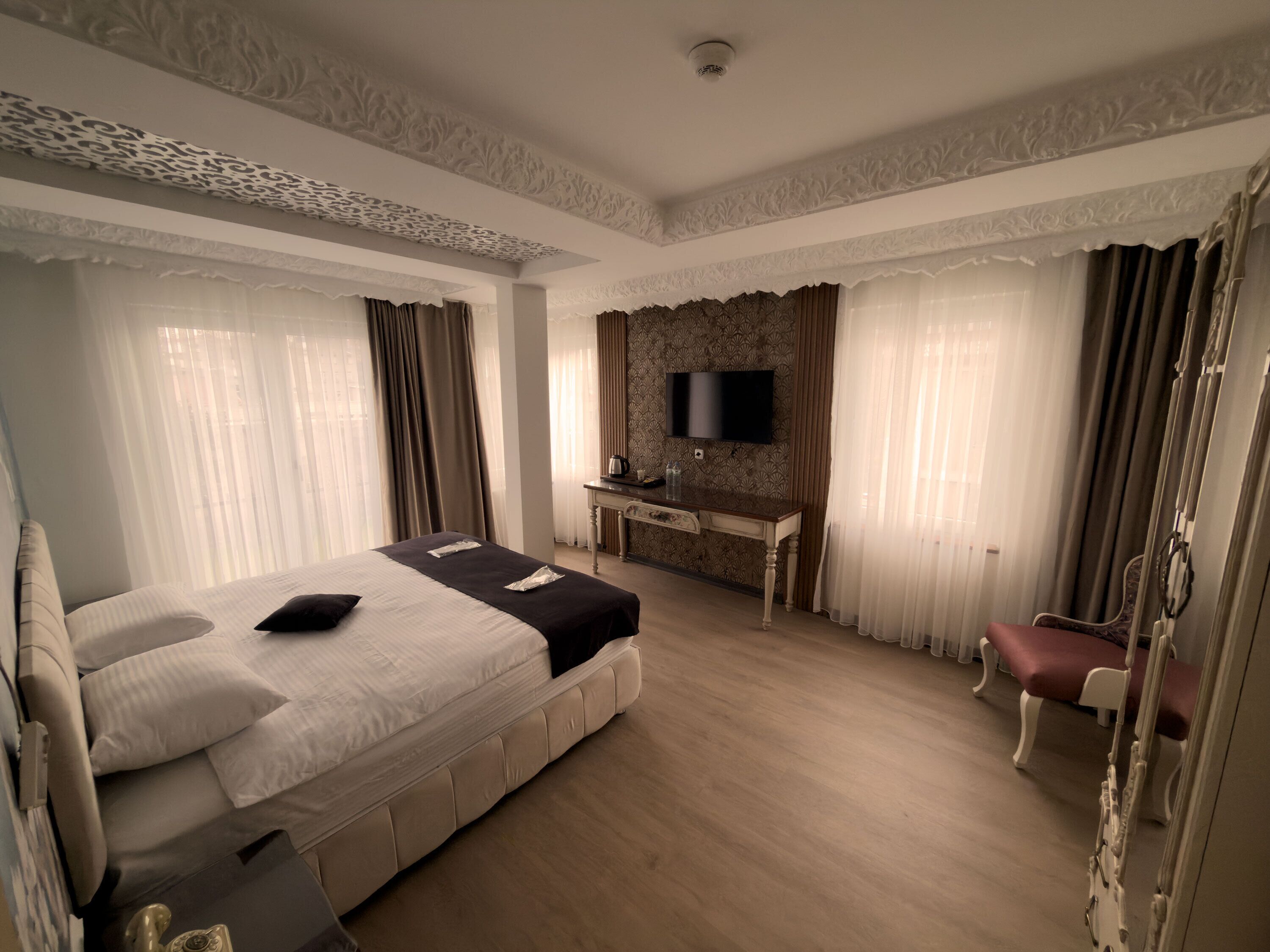 A hotel room with a large bed, a desk with a TV, and a chair.