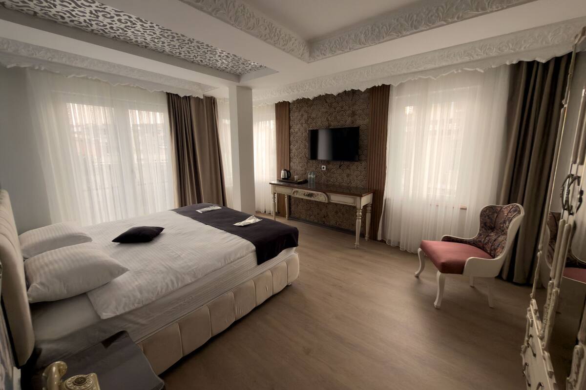 A hotel room with a large bed, a desk, a chair, and a television.