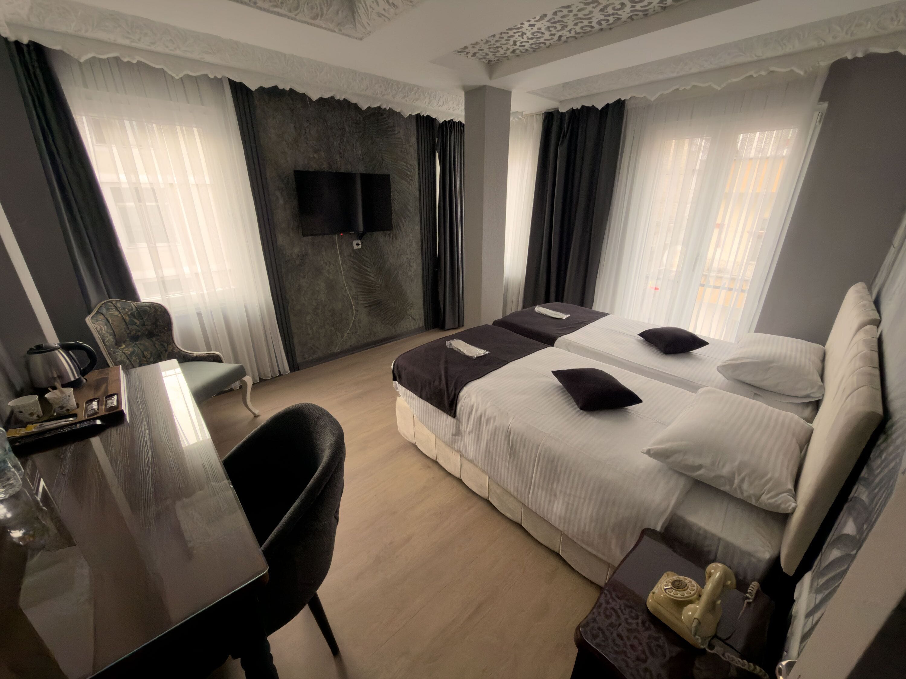A hotel room with a bed, a desk, a chair, a TV mounted on the wall, and a window with curtains.