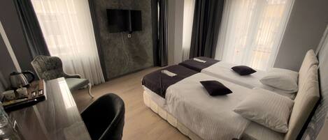Habitación de hotel con cama, escritorio, silla, televisor montado en la pared y ventana con cortinas.