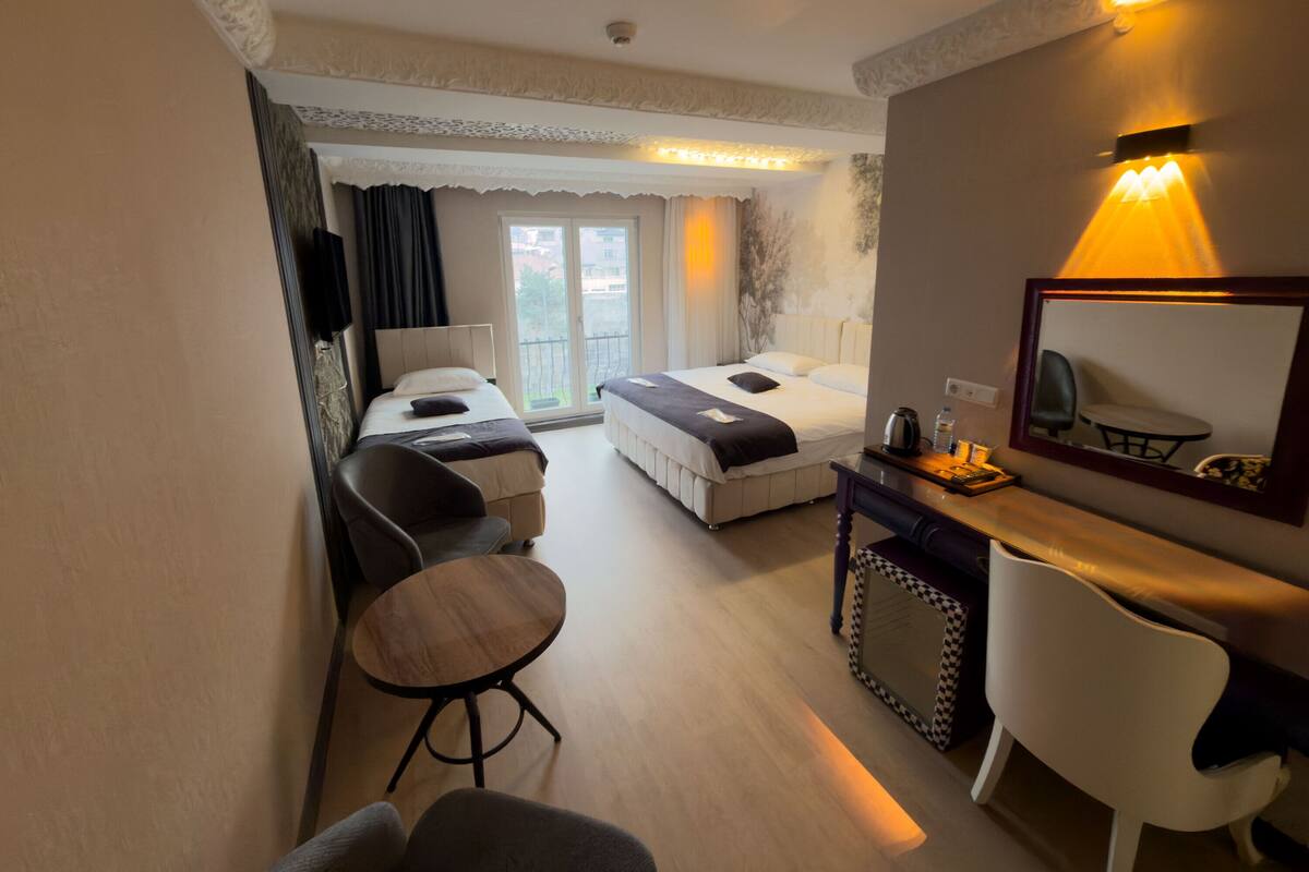 A hotel room with a bed, a desk with a chair, a small table, and a mirror.