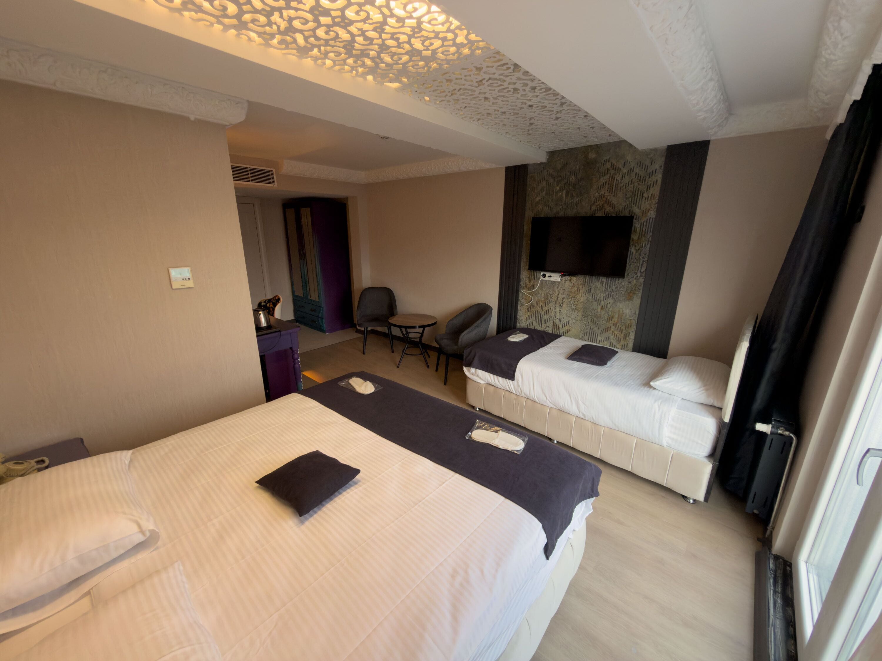 A hotel room with two beds, a desk, a chair, a TV mounted on the wall, and a patterned wall.