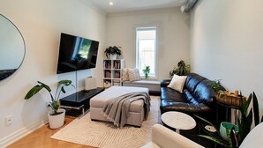 A modern living room with a flat-screen TV, a bookshelf, a sofa, and a coffee table. - Chic Retreat Downtown Meaford 2 min to Georgian bay and ~20 min to ski hills (Meaford)