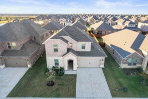 A suburban neighborhood with uniform houses, a central driveway, and a well-maintained lawn. - Luxurious 4-Bed Home in Aubrey TX (Aubrey)