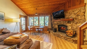 Ein gemütliches Wohnzimmer mit Kamin aus Stein, Holzboden und einem Essbereich mit Tisch und Stühlen.