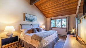 Ein Schlafzimmer mit einem großen Bett, Nachttischlampen, einem hölzernen Kopfteil, einem Fenster mit Vorhängen und einem Bild an der Wand.