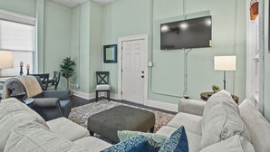 A living room with a sofa, ottoman, and a flat-screen TV mounted on the wall. - Local Discounts-Charming View of Downtown Newark (Newark)