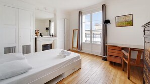 A bedroom with a bed, a dresser, a desk, a fireplace, a large window with curtains, and a painting on the wall. - Top floor Saint Germain Terrace Apartmrent (Paris)