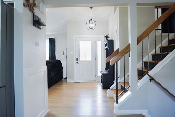 A hallway with a staircase, a door, and a hanging light fixture.