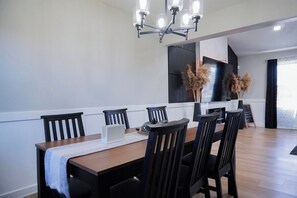 Een eetruimte met een houten tafel, zwarte stoelen, een laptop en een kroonluchter.