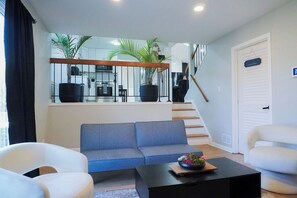 Un salon moderne comprenant un canapé, des fauteuils, une table basse et un escalier menant à un deuxième étage.