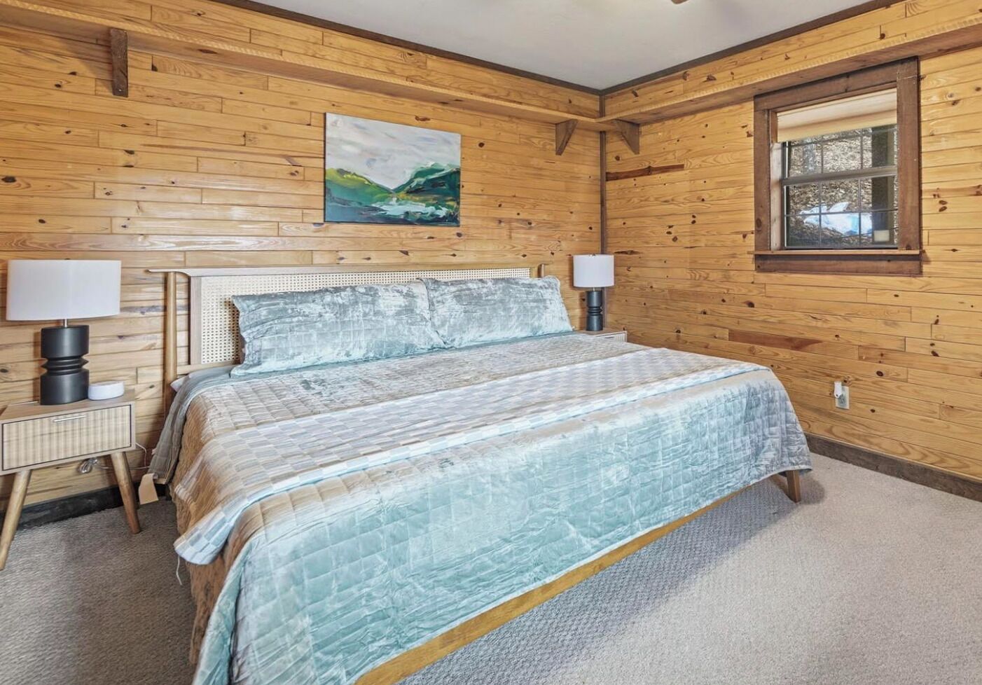 A wooden-paneled bedroom with a bed, two bedside lamps, a painting, and a window.