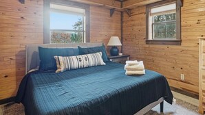 Een slaapkamer met houten lambrisering, een bed, kussens, een nachtkastje en een lamp.