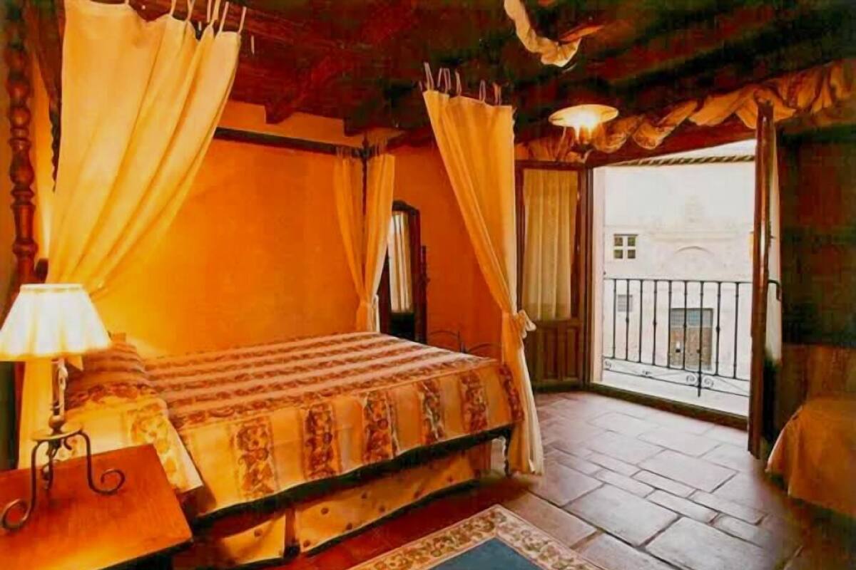 Een slaapkamer met een bed, gordijnen, een nachtkastje en uitzicht op het buiten.