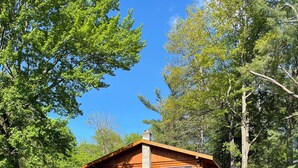 A log cabin with a balcony, surrounded by lush greenery and trees. - Wisconsin River Getaway. Large yard and shoreline. Pet friendly. (Merrill)