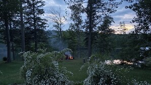 A serene outdoor setting with a fire pit surrounded by lush greenery and tall trees. - Wisconsin River Getaway. Large yard and shoreline. Pet friendly. (Merrill)