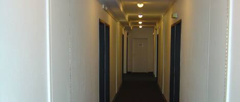 A long, narrow hallway with white walls and a dark carpet.