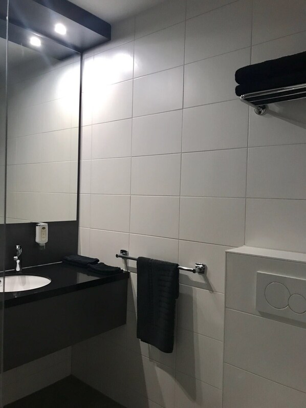 Un baño moderno con un lavabo negro, un espejo y un perchero para toallas.